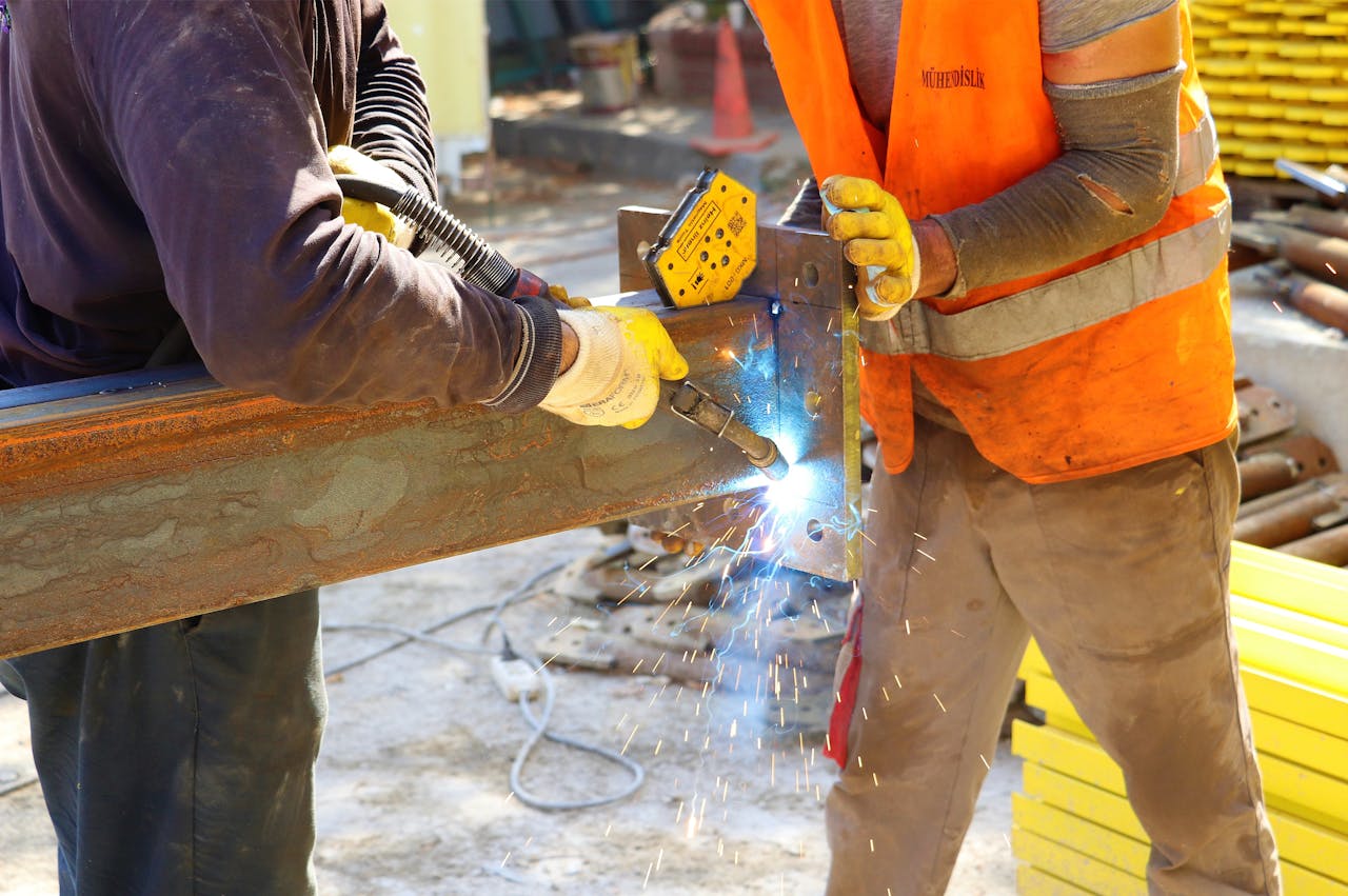 about-02 Two workers in safety gear welding metal at a construction site, emitting sparks.
