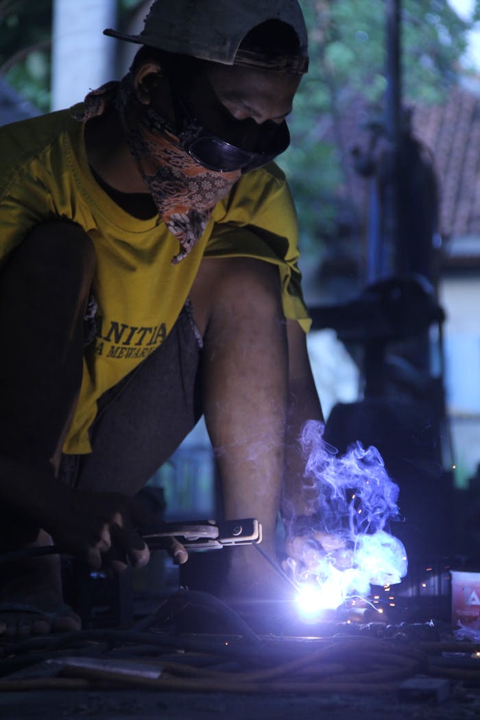 gallery-5 A worker skillfully welding metal in a workshop, wearing protective gear and creating sparks.