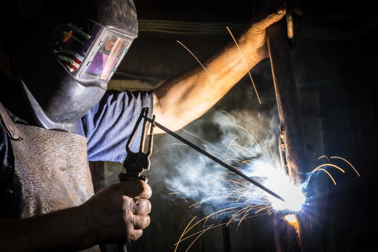 hero-img-01 Close-up of a welder in action, showcasing bright sparks and metalworking skill indoors.